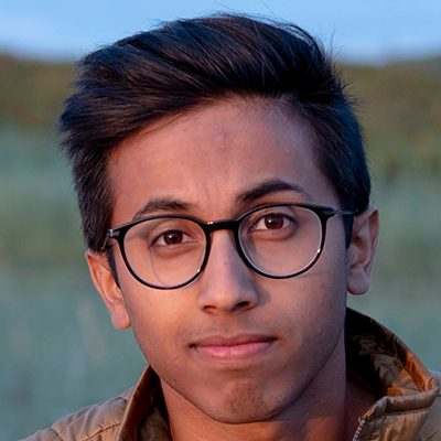 Aman, a person with brown skin and short black hair, wearing glasses.