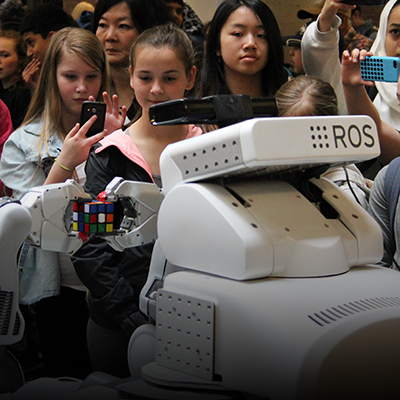 A group of middle and high school students watches a robot solve a Rubik's Cube.
