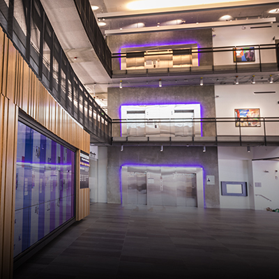 Interior of the Gates Center atrium showing multimedia display on wall and multiple floors of purple-lit elevator banks