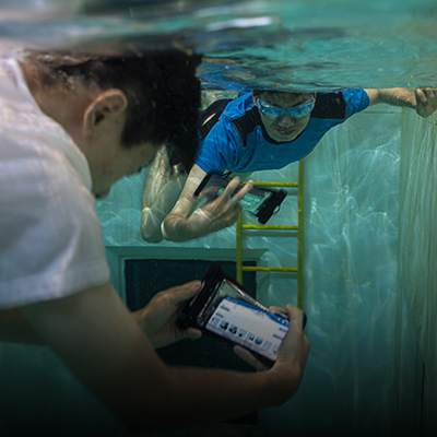 Two students underwater testing AquaApp diving app on their smartphones within waterproof cases