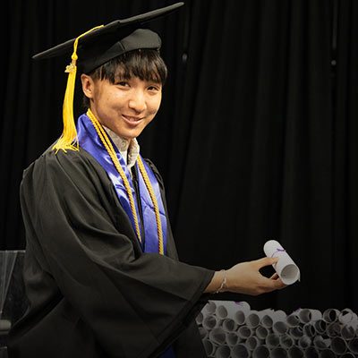 A student wearing a cap and gown, accepting their diploma at graduation celebration