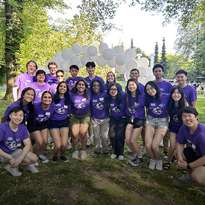 Undergraduate students wearing matching purple shirts gather outside for a group photo.