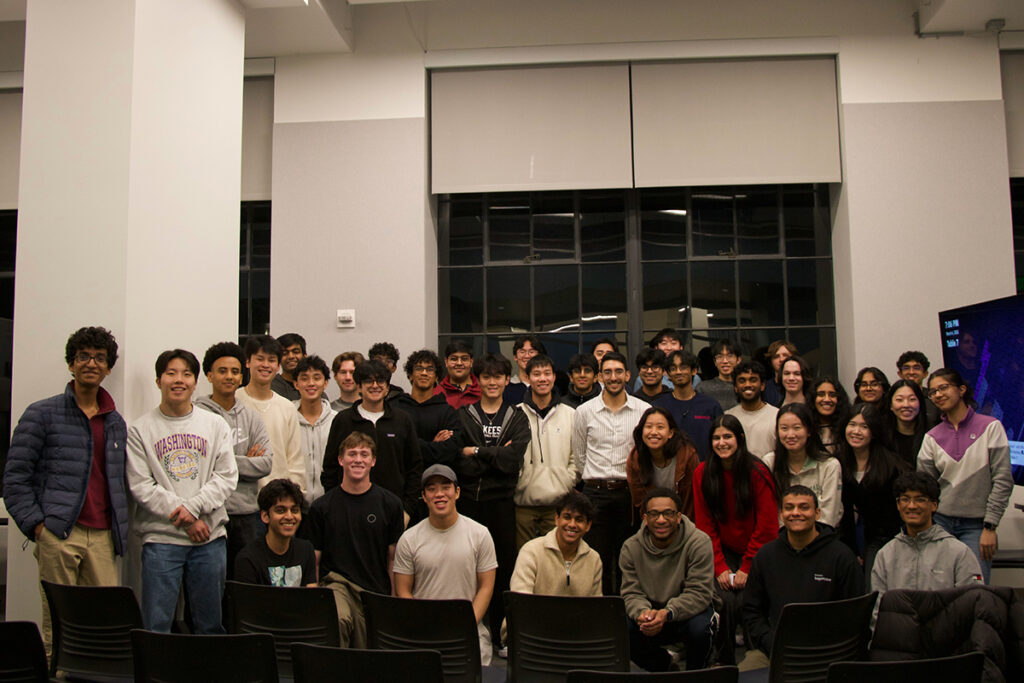 A large group of students pose with Armon Dadgar in a high-ceilinged room