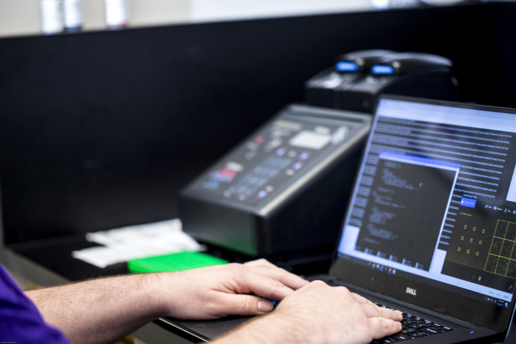 Trusted Computing Systems Grand Challenge: Hands typing on qa laptop keyboard with code displayed on the screen.