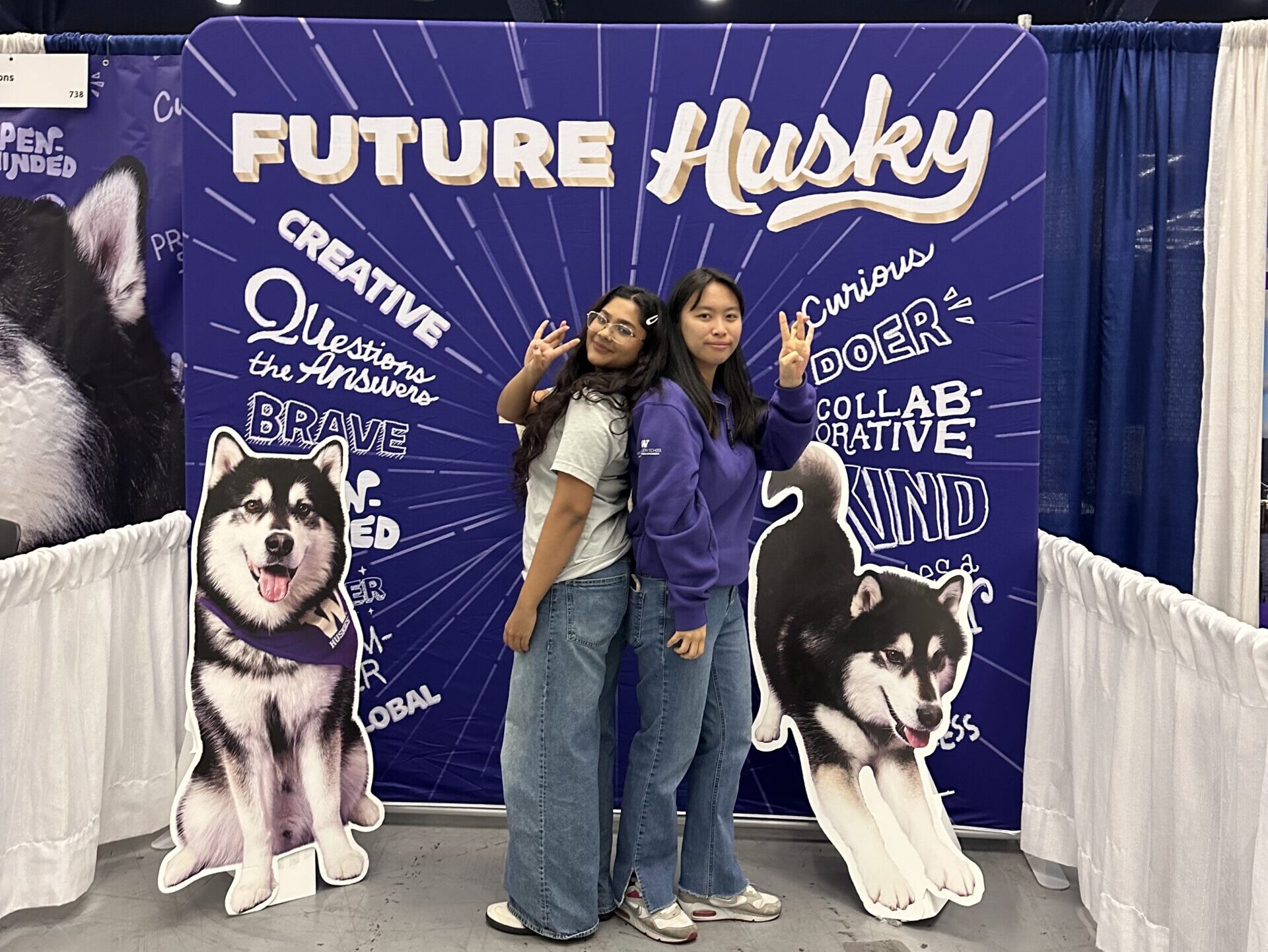 Two Allen School Student Recruitment Representatives hold their "Dubs Up" fingers in front of a "Future Huskies" sign