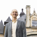 Ed Lazowska standing in front of an old university building that resembles a castle with turrets and stained glass