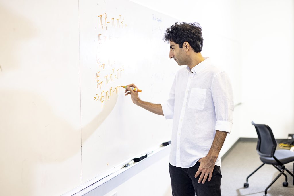 Shayan Oveis Gharan shown in profile, writing an equation on a whiteboard
