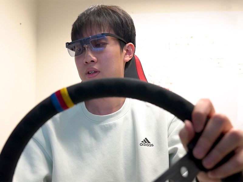 Student wearing goggles and seated behind the wheel of a driving simulator while participating in a study of distracted driving