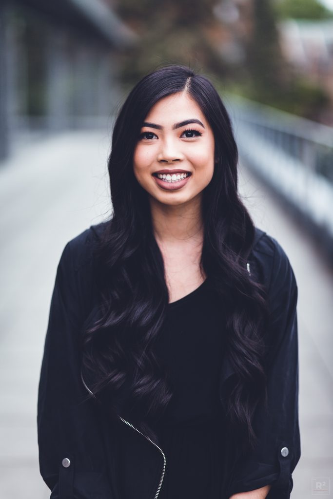 Rose smiling and standing outdoors, wearing a black jacket and blouse. 