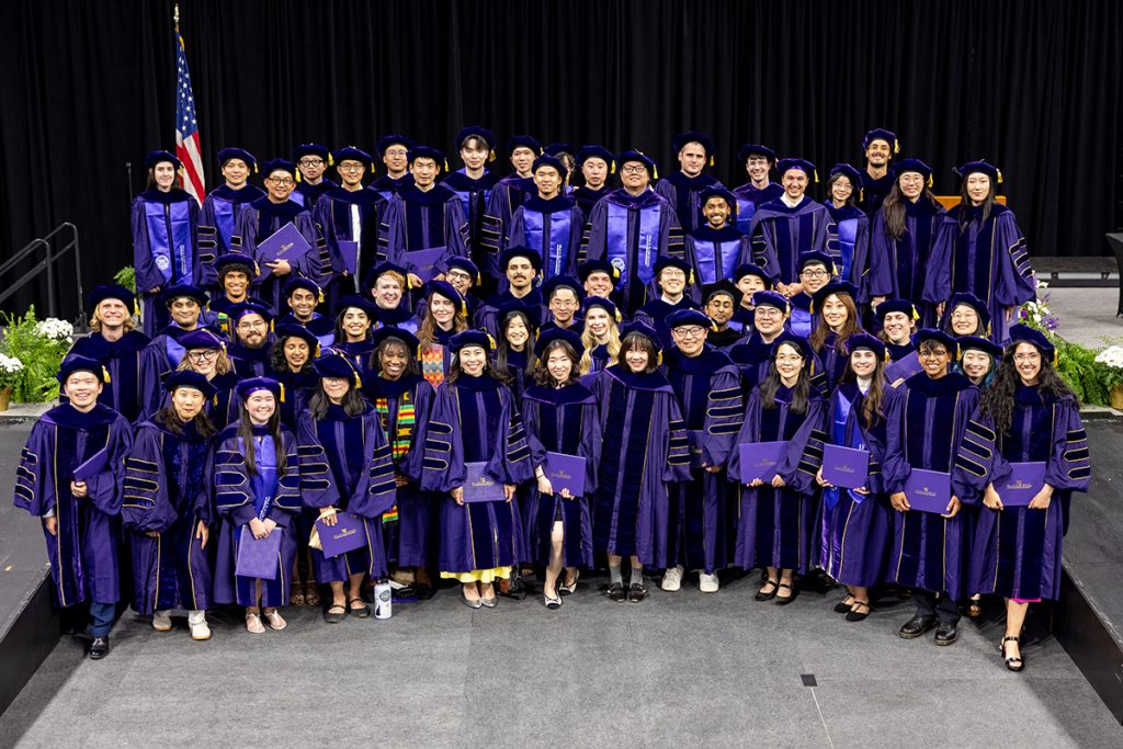 Large group of Ph.D. graduates posing with commemorative diplomas in their UW graduation regalia