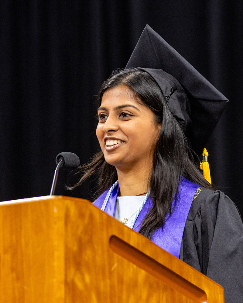 Closeup of Vaishnavi Vidyasagar in cap and gown smiling from behind the podium