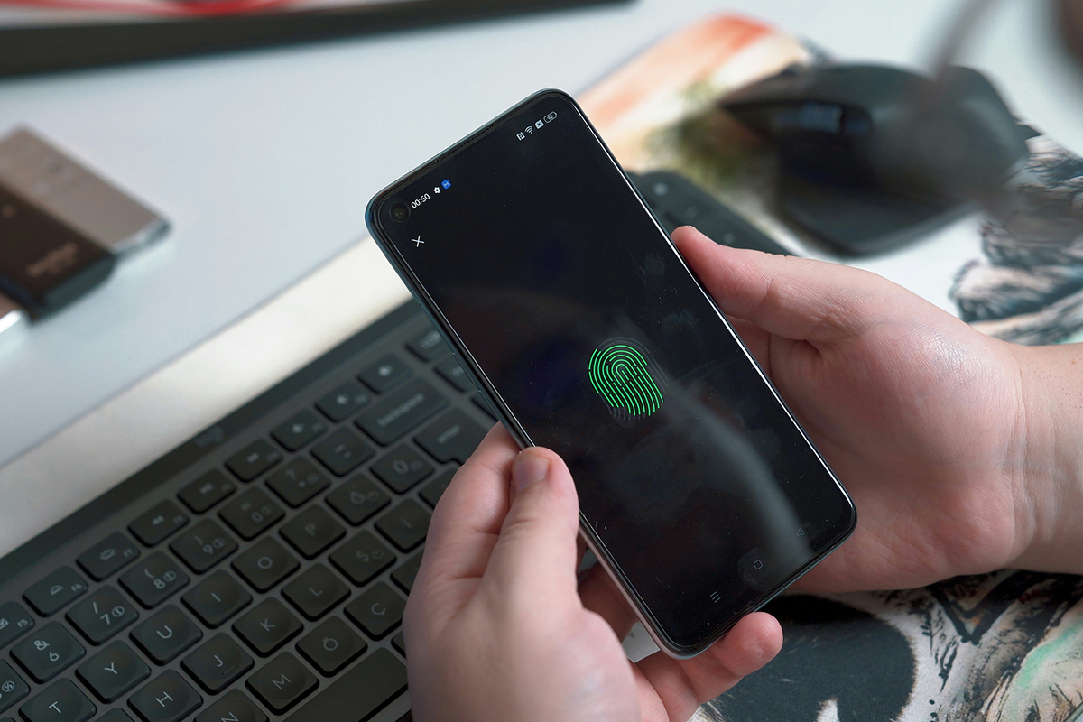 A person holds a smartphone in their hands. The smartphone screen shows a green fingerprint.