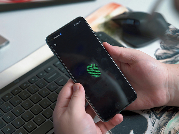 A person holds a smartphone in their hands. The smartphone screen shows a green fingerprint.