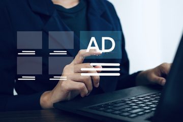 Person in blue shirt on a laptop points at ads coming off their screen.