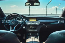 The view through the windshield of a car showing the black leather interior and blue skies through the windshield.