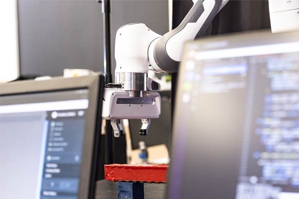 Photo of a robotic arm with two computer screens featuring code in front of it.