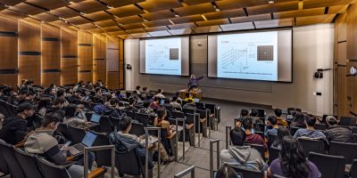 Photo of an Paul G. Allen School professor teaching class in an auditorium with large screens.