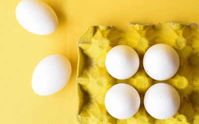 A yellow carton full of white eggs sits against a yellow background.