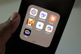 Hand holding smartphone displaying AI chatbot apps, including ChatGPT, DeepSeek, Claude, Mistral AI, Gemini, Copilot and Poe
