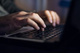 Hands typing at a laptop shrouded in darkness