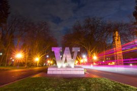 Block W statue at entrance to University of Washington campus flanked by pink and white light streams from moving vehicles at night