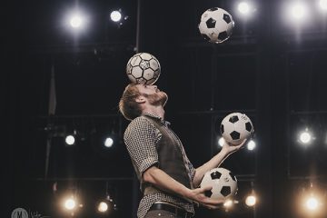 Cory Black juggling four soccer balls on a brightly lit stage