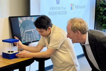 Brad Smith peers over a person's shoulder as they demonstrate a device that uses sound waves to levitate liquid droplets