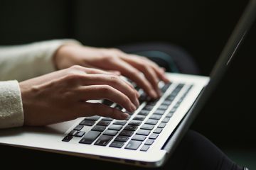 A person's hands and wrists are visible typing on a laptop keyboard.