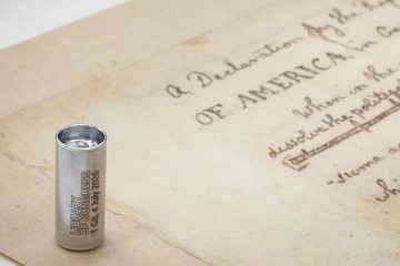 Small metal vial juxtaposed with a paper copy of the draft Declaration of Independence