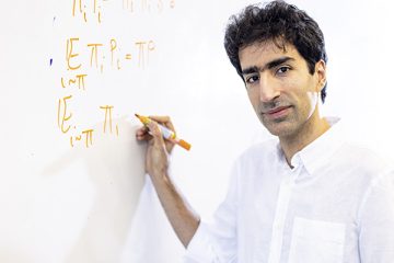 Shayan Oveis Gharan pauses to look at camera while writing on a whiteboard