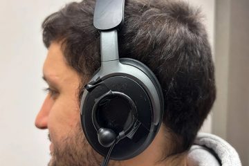 Close-up of a person wearing headphones with a small earbud taped to the exterior of the headphone speaker