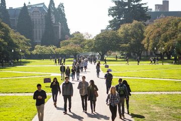 Students walking on the brick path of a sunlit UW quad framed by trees
