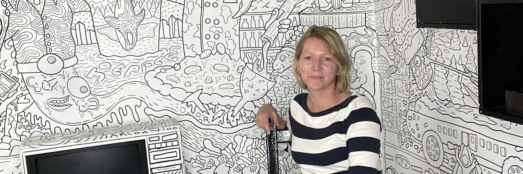 Portrait of Katharina Reinecke in a room decorated with wallpaper displaying black and white line drawings